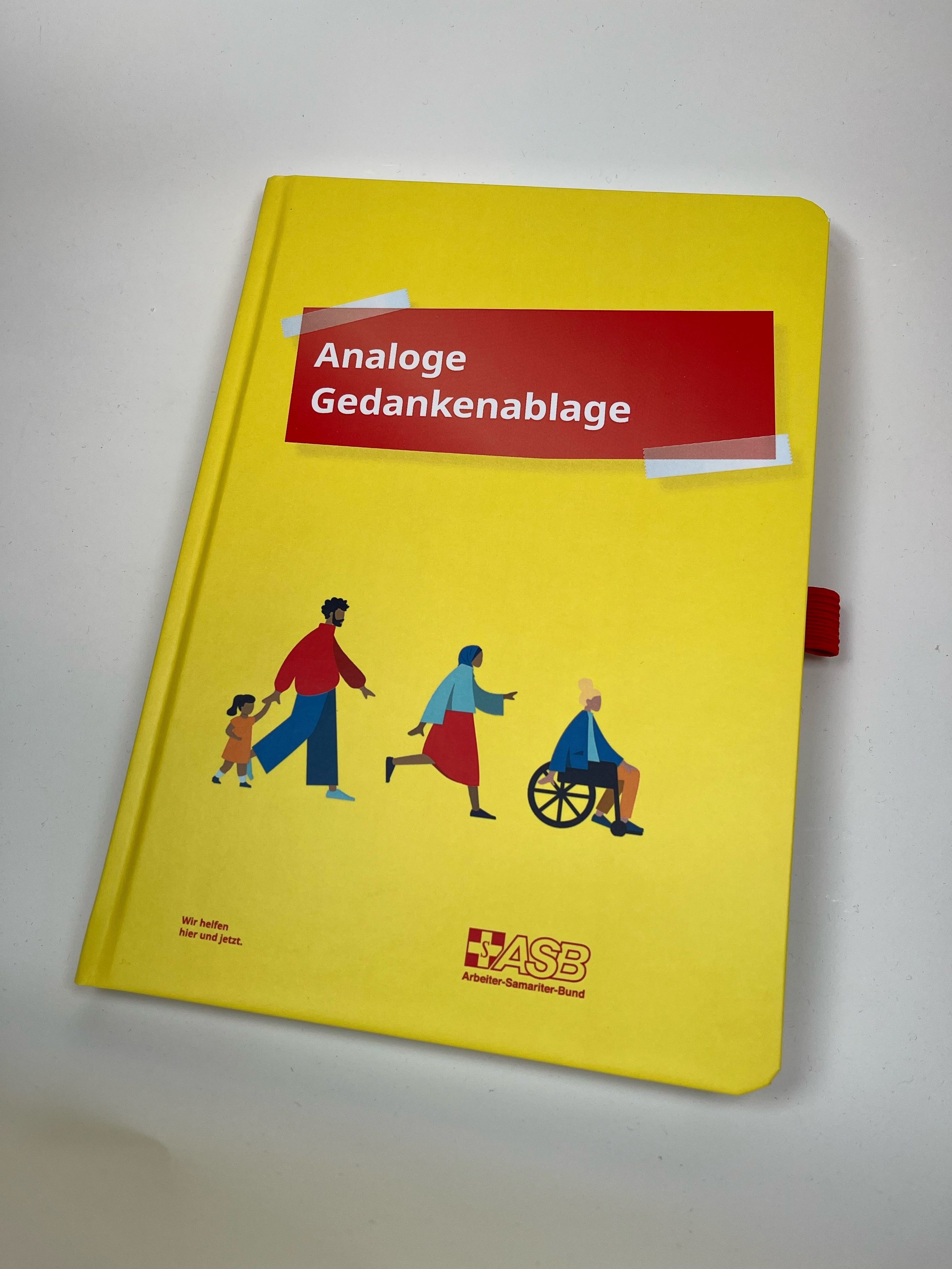 Notizbuch "Analoge Gedankenablage" Gelbes Notizbuch mit Titel „Analoge Gedankenablage“, ASB-Logo und Illustrationen von Menschen in Bewegung, inkl. Rollstuhlfahrer.