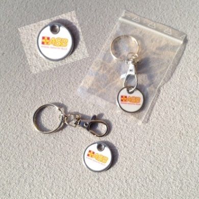 Drei Einkaufswagenchips mit ASB-Logo, je mit Schlüsselring und Karabiner, einer davon in transparenter…